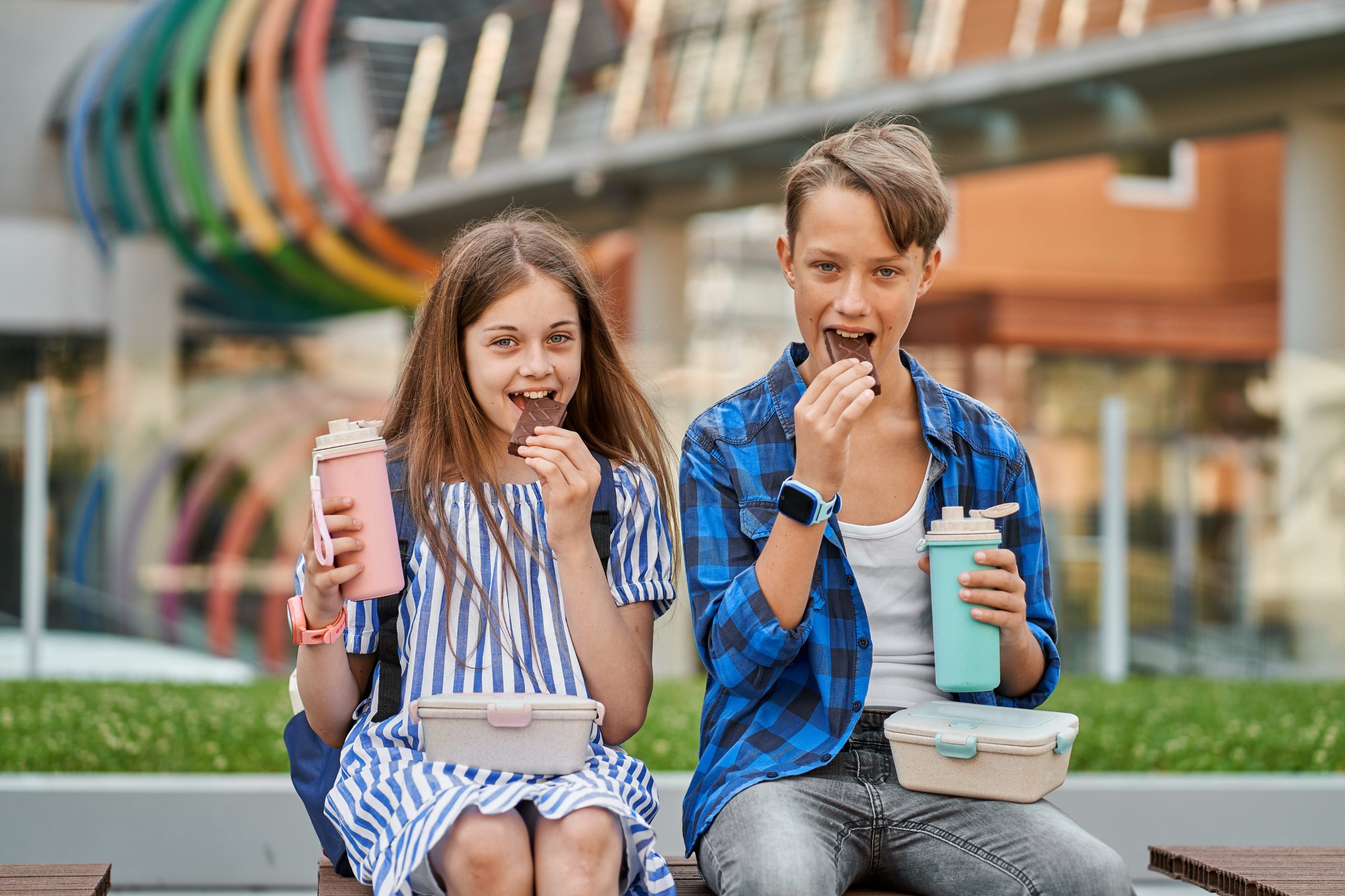 Two students around 12 y.o. a boy and a girl seen eating bars of chocolate outside their school.